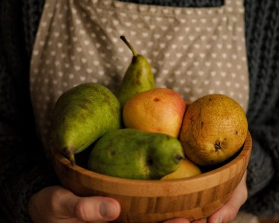 Close-up of a person holding a wooden bowl with fresh fruits including pears.